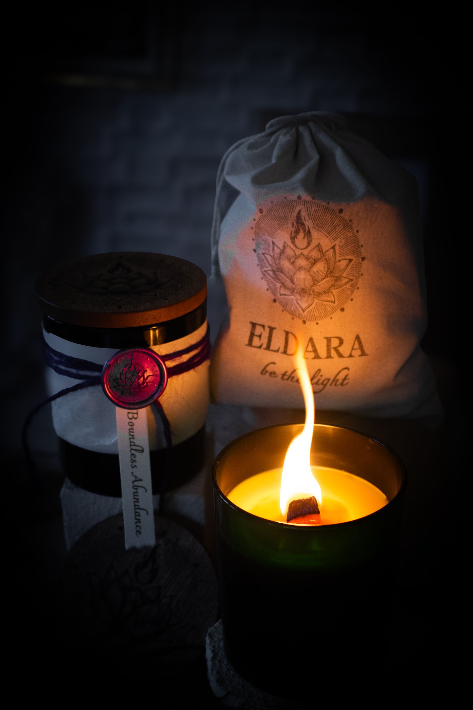 Boundless Abundance candle by Eldara, shown with its sealed wooden lid and cotton canvas bag. A ritual candle infused with green aventurine and sacred intention.