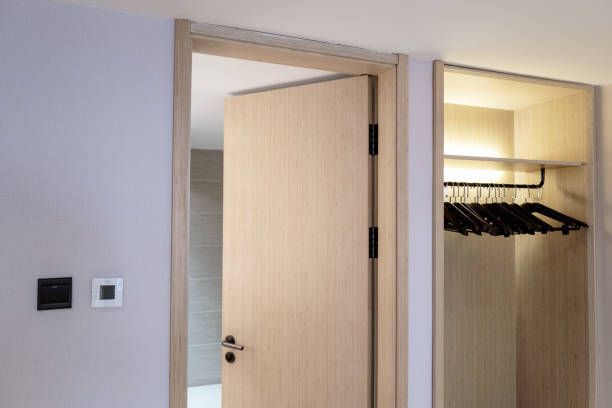Partially open wooden door with black hardware next to a lit closet with hangers.