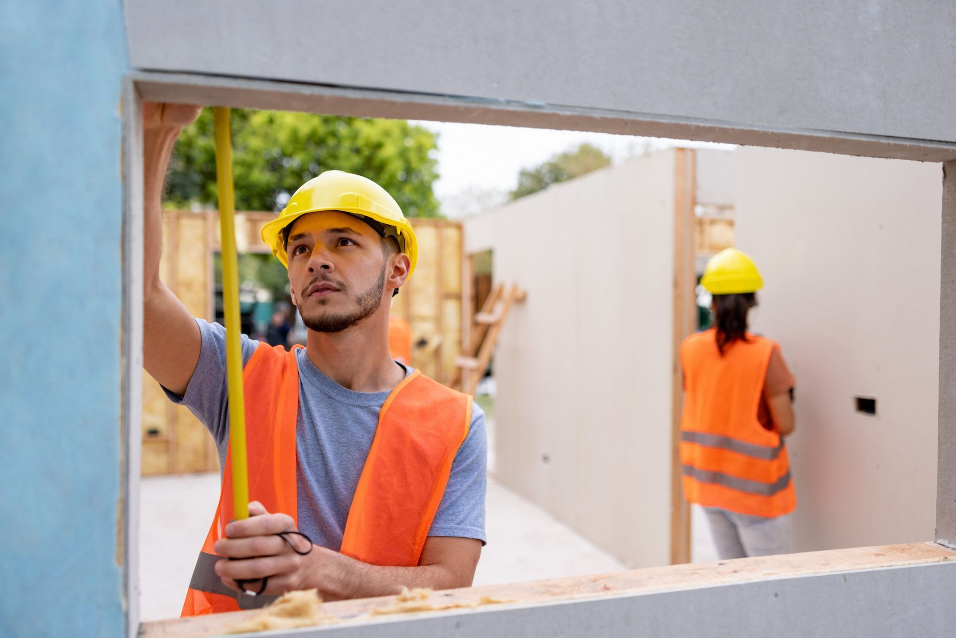 Workers measure window opening at unfinished building site.