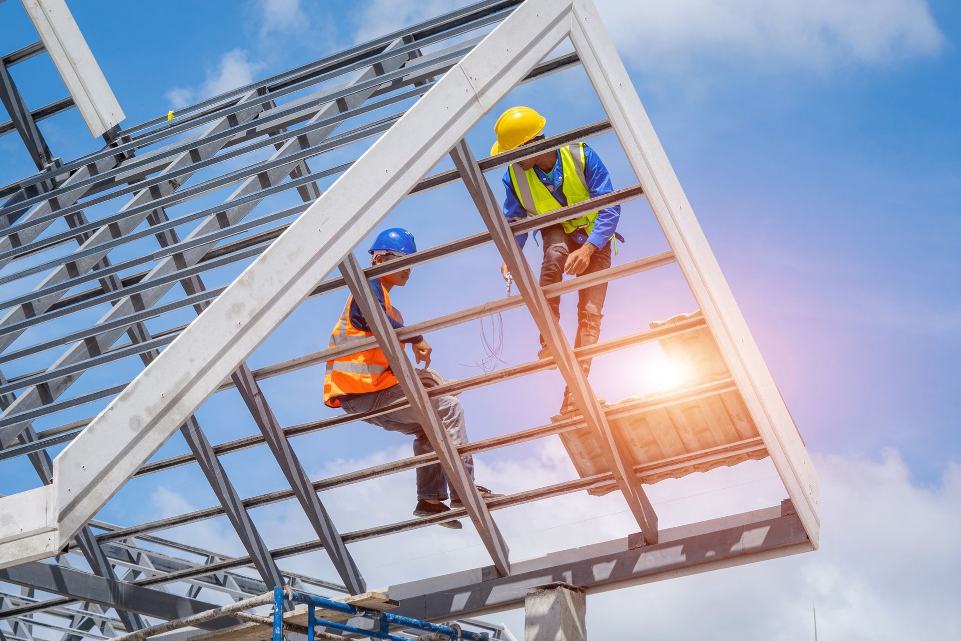 Construction workers assembling a metal roof frame under a bright sky.