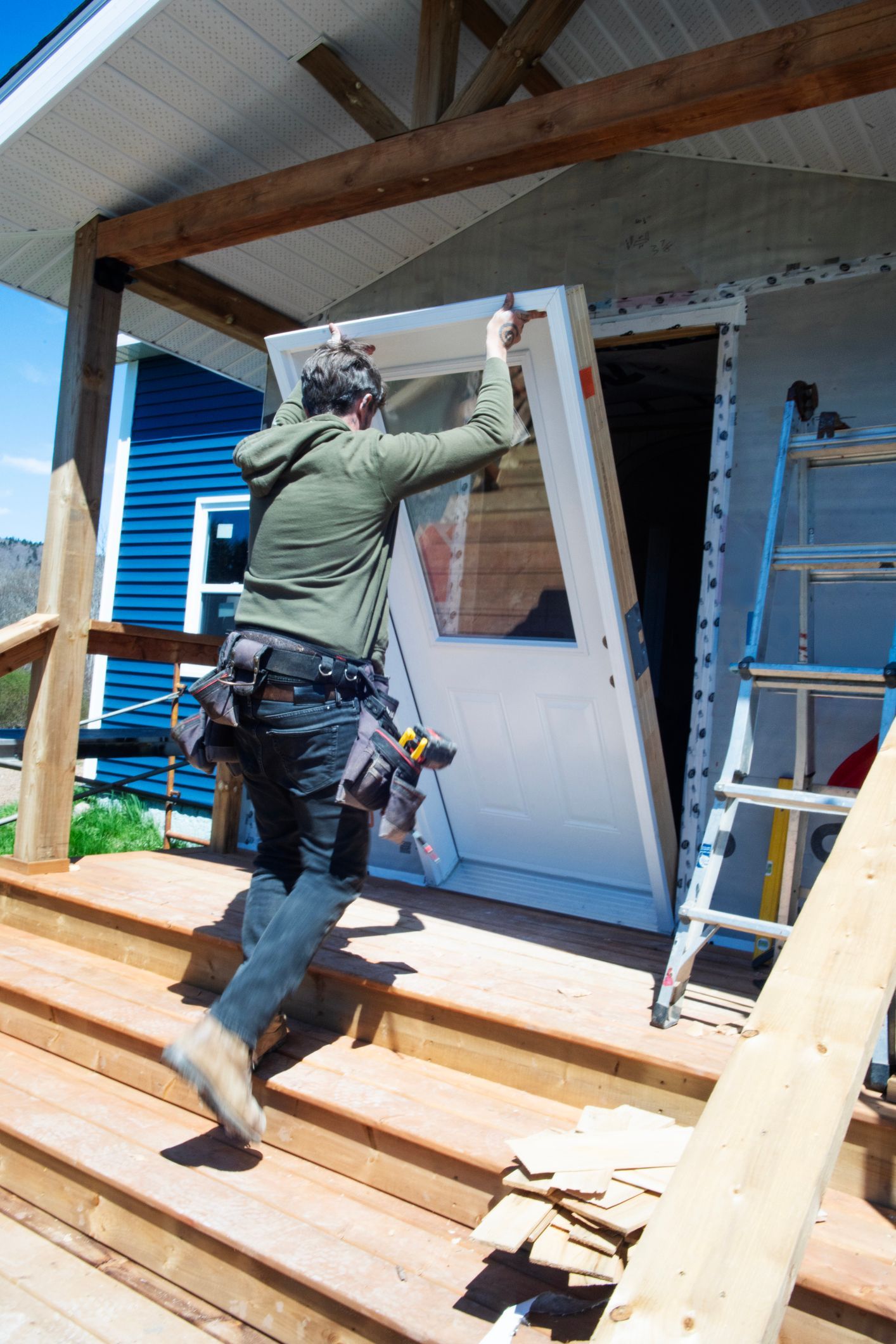 A mid-adult male contractor installing a new white entry door during a renovation on an older home. A mid-adult male contractor installing a new white entry door during a renovation on an older home.