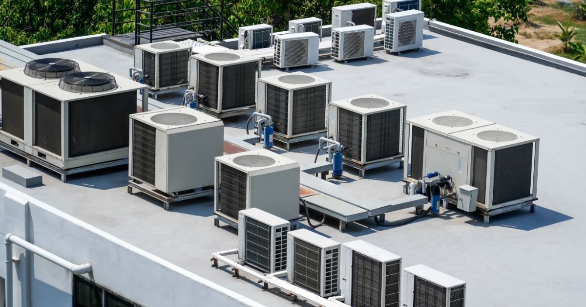 A flat commercial rooftop has white roofing material and several HVAC units installed. Trees surround the building.