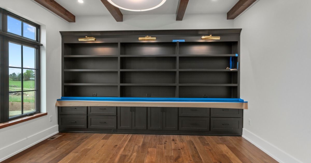 A built-in wall unit spans the width of a room. It has empty open shelves above and closed drawers and cabinets below.