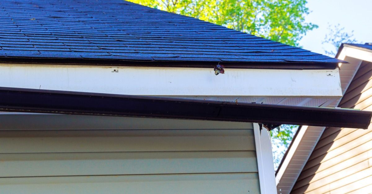 A roof edge shows a gutter section completed detached from a white fascia board. The roof has dark shingles.