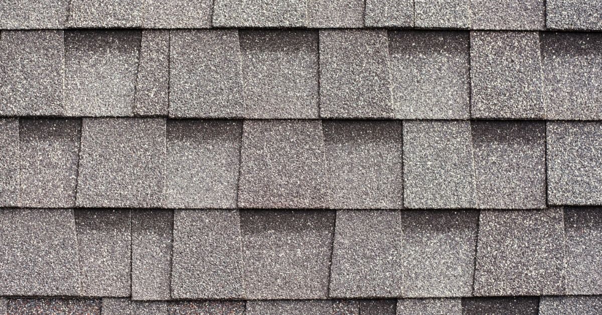 Close-up of gray architectural asphalt roof shingles. The rectangular tabs are staggered and overlap in horizontal rows.