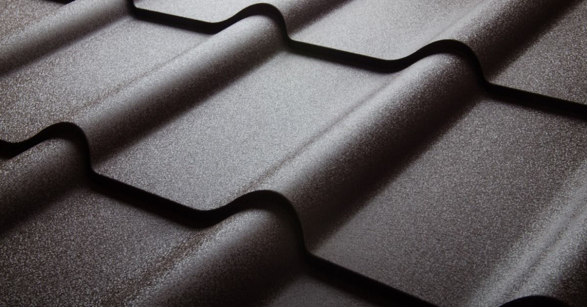 Close-up view of dark gray metal roof shingles with a raised, wavy profile. The textured surface reflects light.