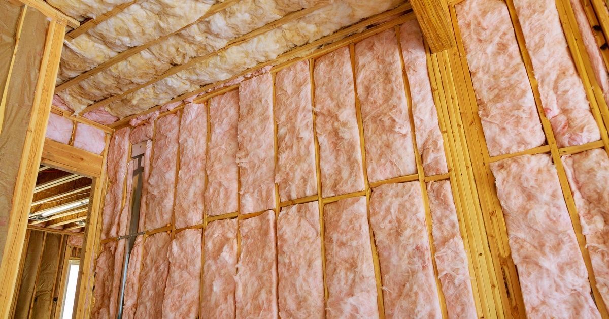 Fluffy fiberglass insulation fills the spaces between interior wooden wall studs and between exposed ceiling beams.