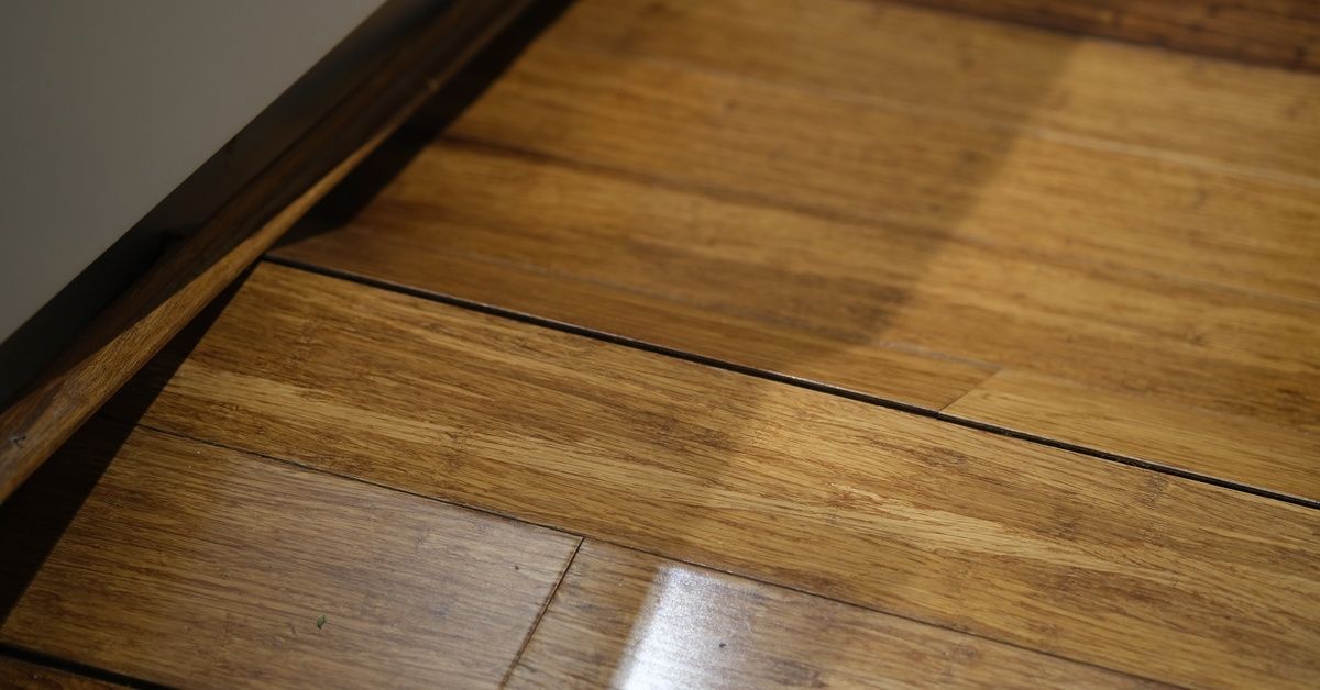 A close-up of a floor made of narrow planks with a glossy finish and color variation. Some planks do not lie flat.