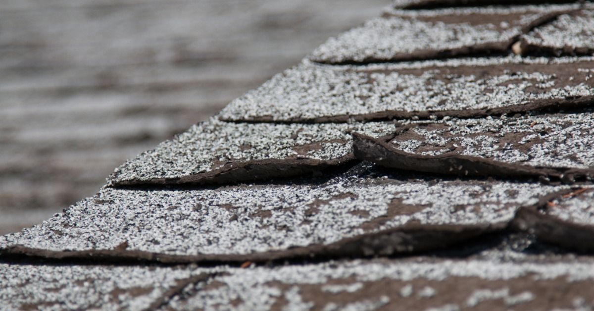 Close-up of brown asphalt shingles that are uneven, worn, and lifting.