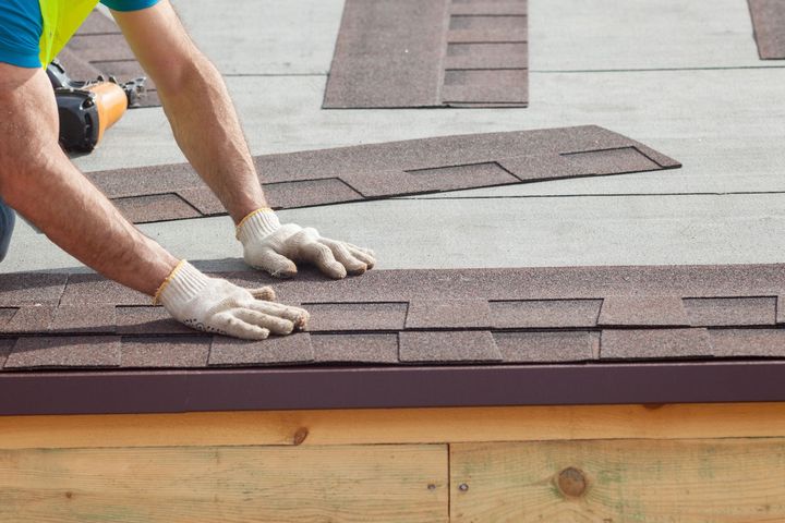 Close-up of a roofing contractor, wearing gloves and on top of a roof, installing roof shingles.