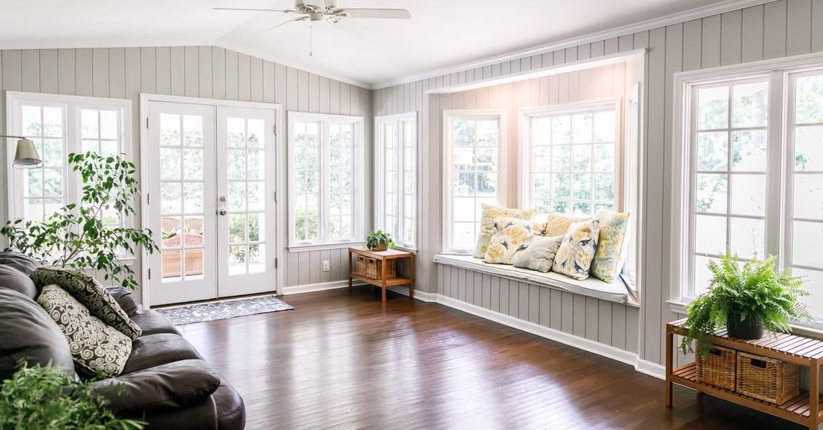 A bright sunroom with wall-to-wall windows, a window bench with throw pillows, French doors, and warm wood flooring.