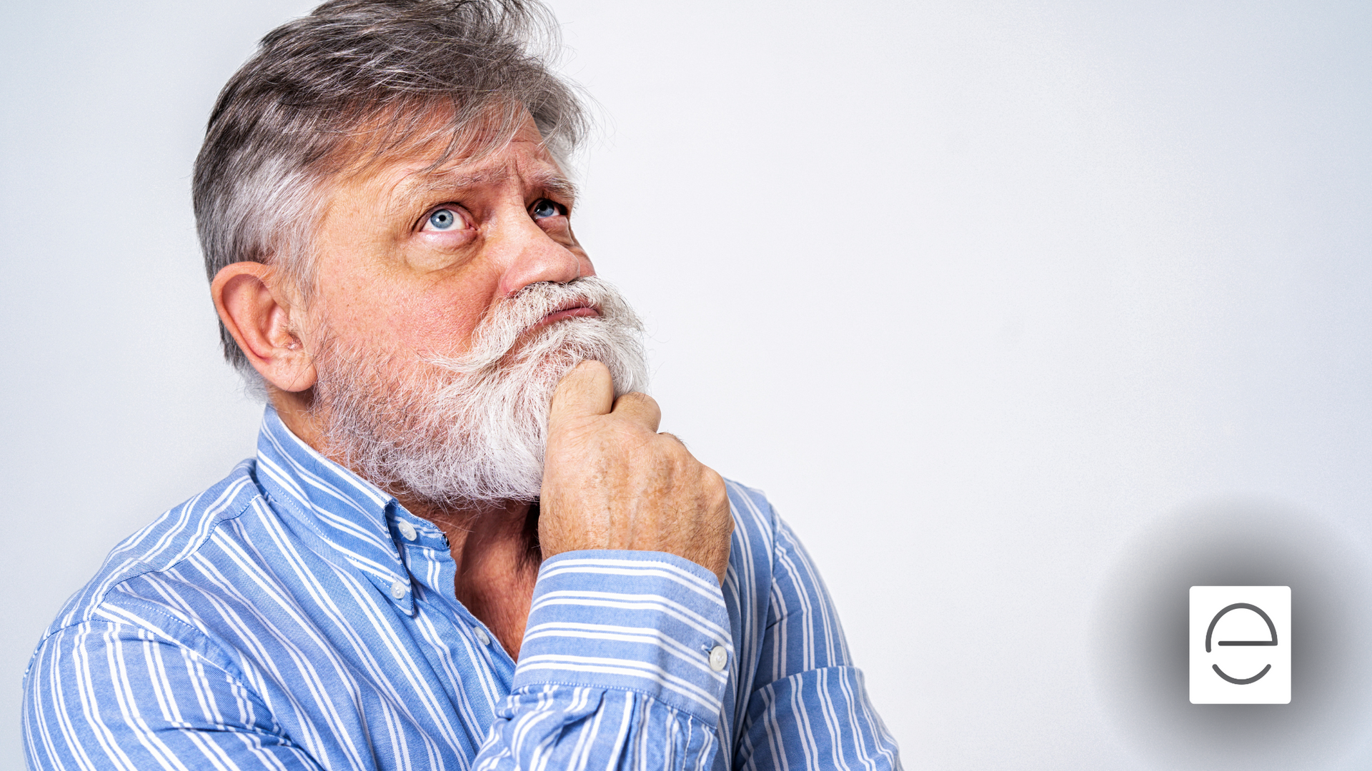 A man with a beard and a blue striped shirt is thinking.