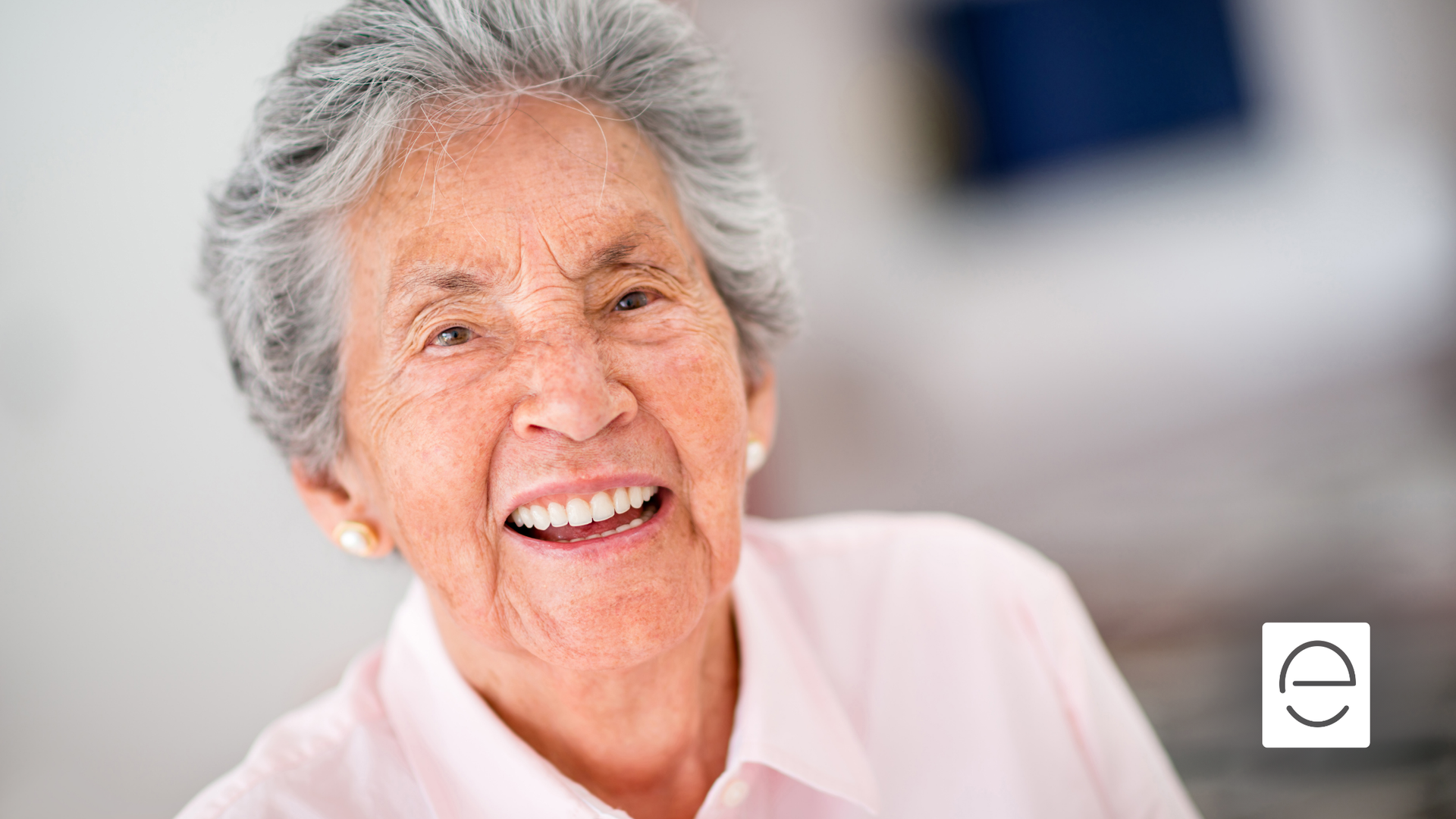 An elderly woman is smiling for the camera while wearing a pink shirt.