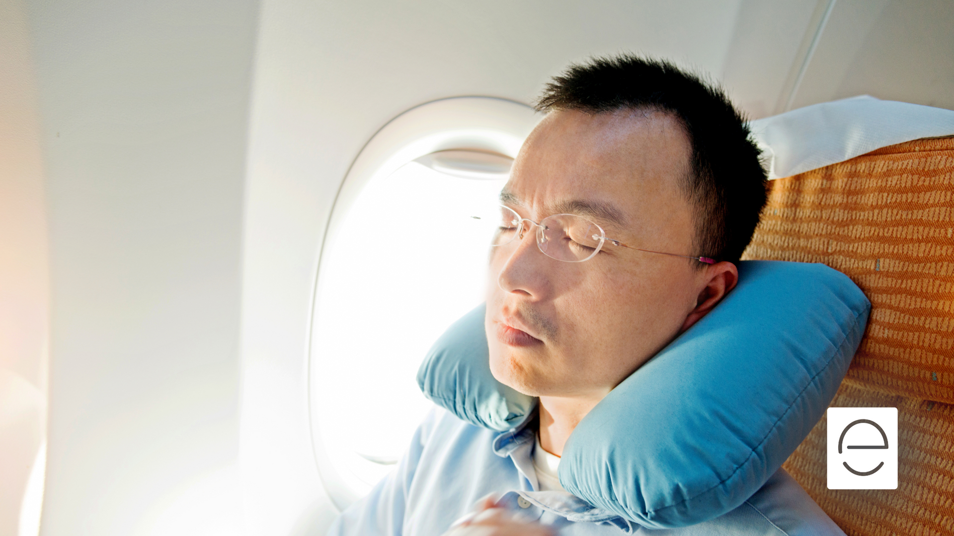 A man is sleeping on an airplane with a neck pillow around his neck.