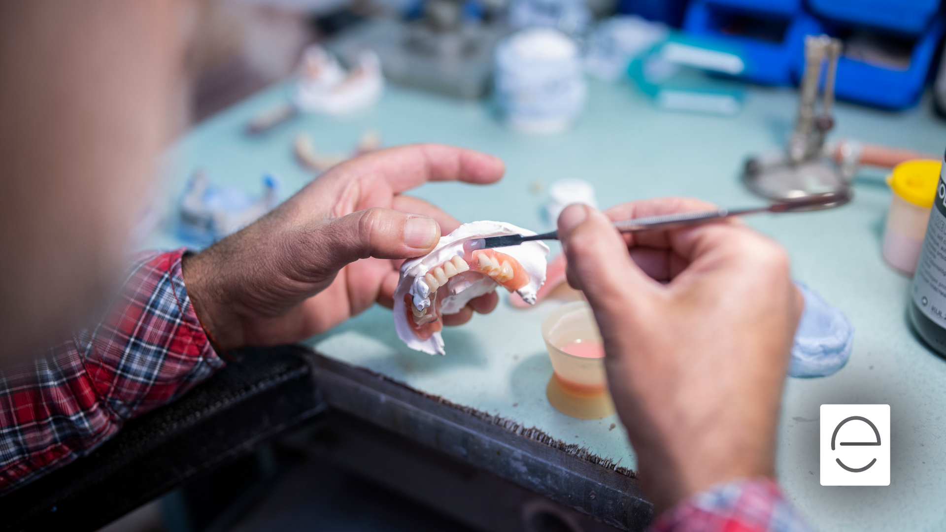 A dentist is working on a denture with a brush.