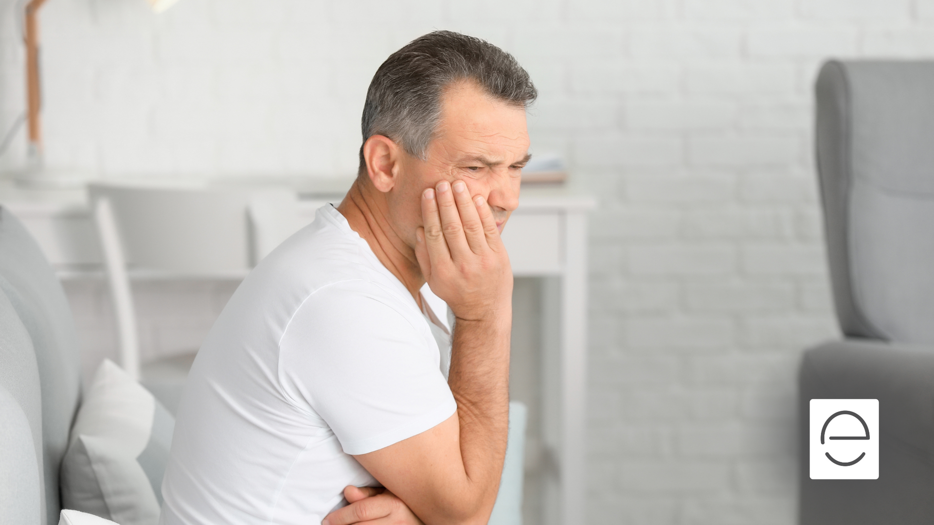 A man is sitting on a couch with his hands on his face.