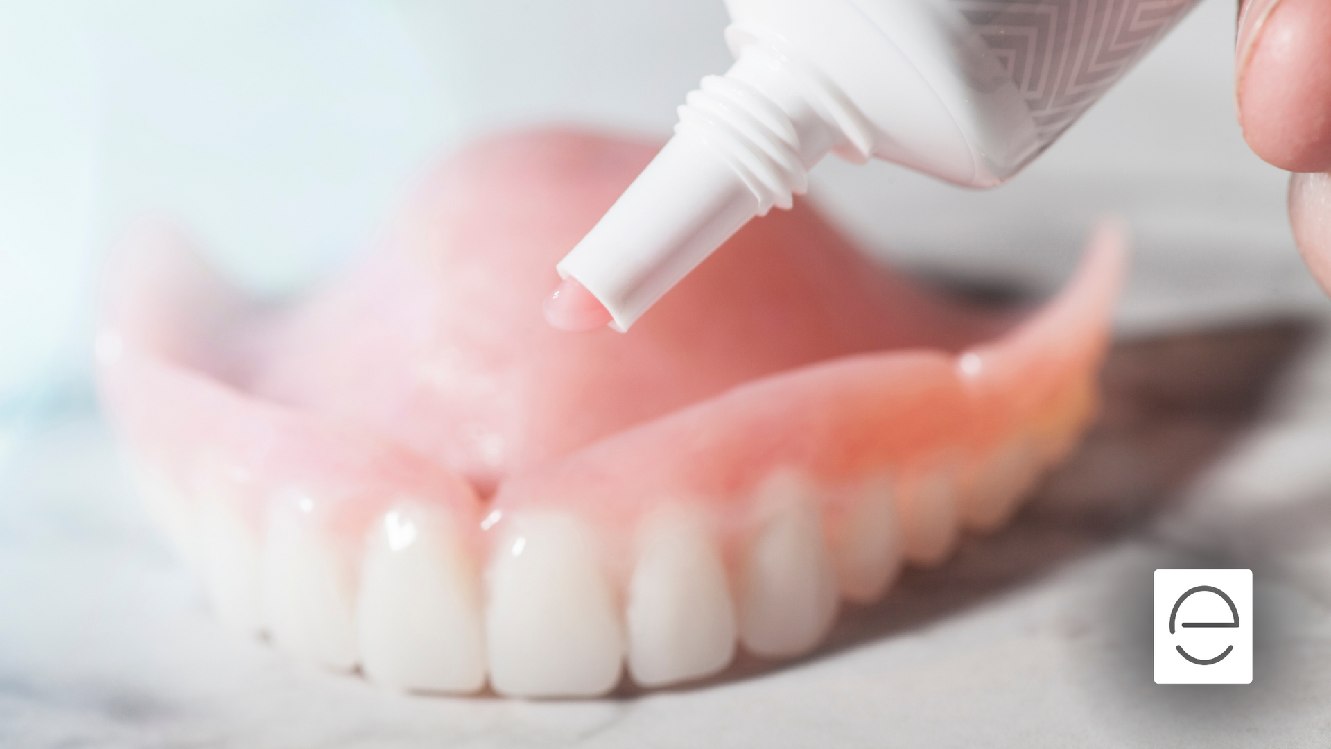 A person is applying toothpaste to a denture.