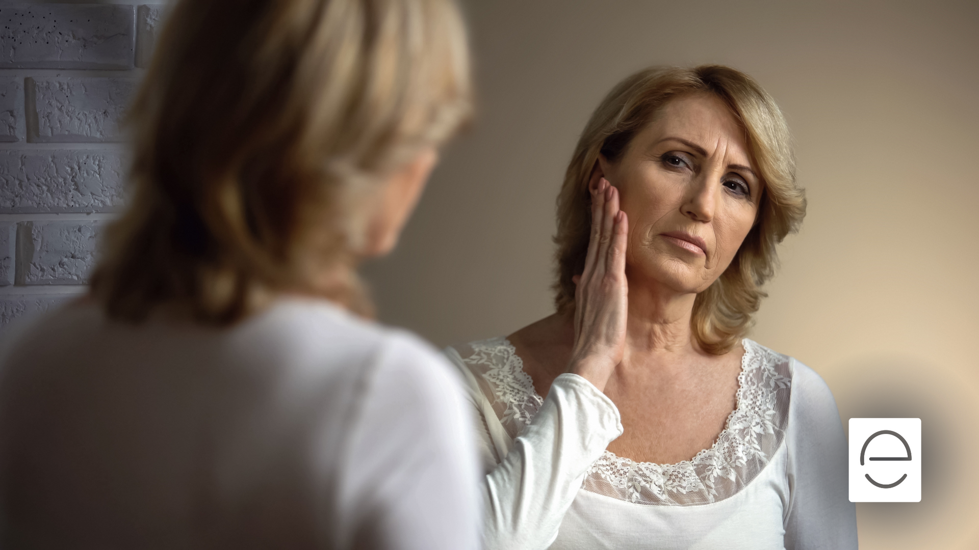 A woman is looking at her face in a mirror.