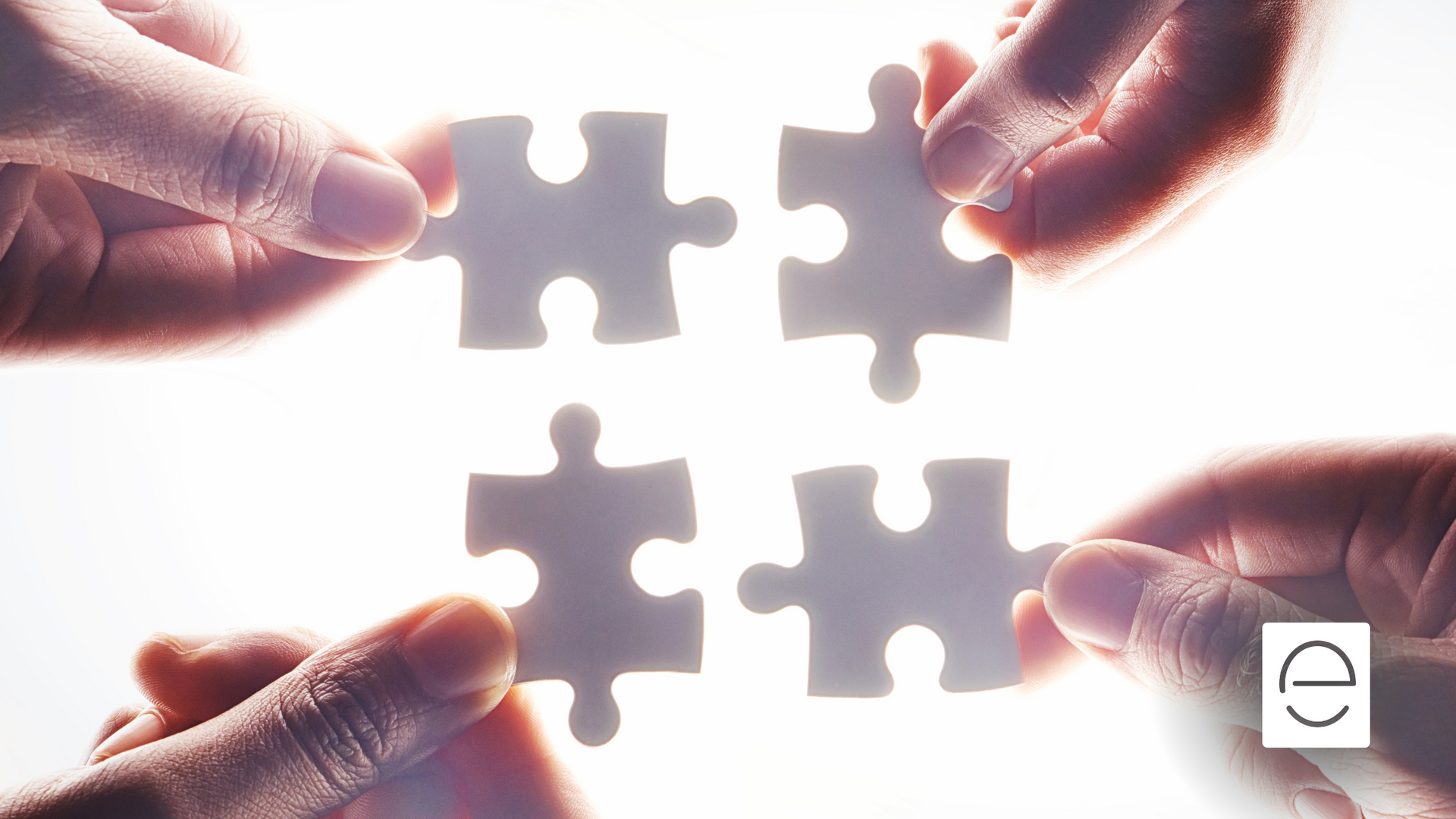 A group of people are holding four puzzle pieces together.