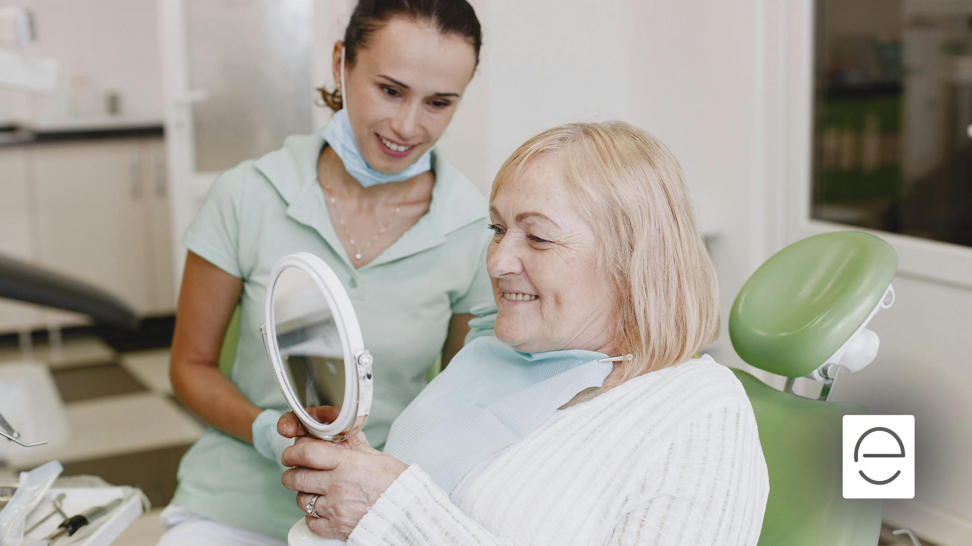 A woman is sitting in a dental chair looking at her teeth in a mirror.