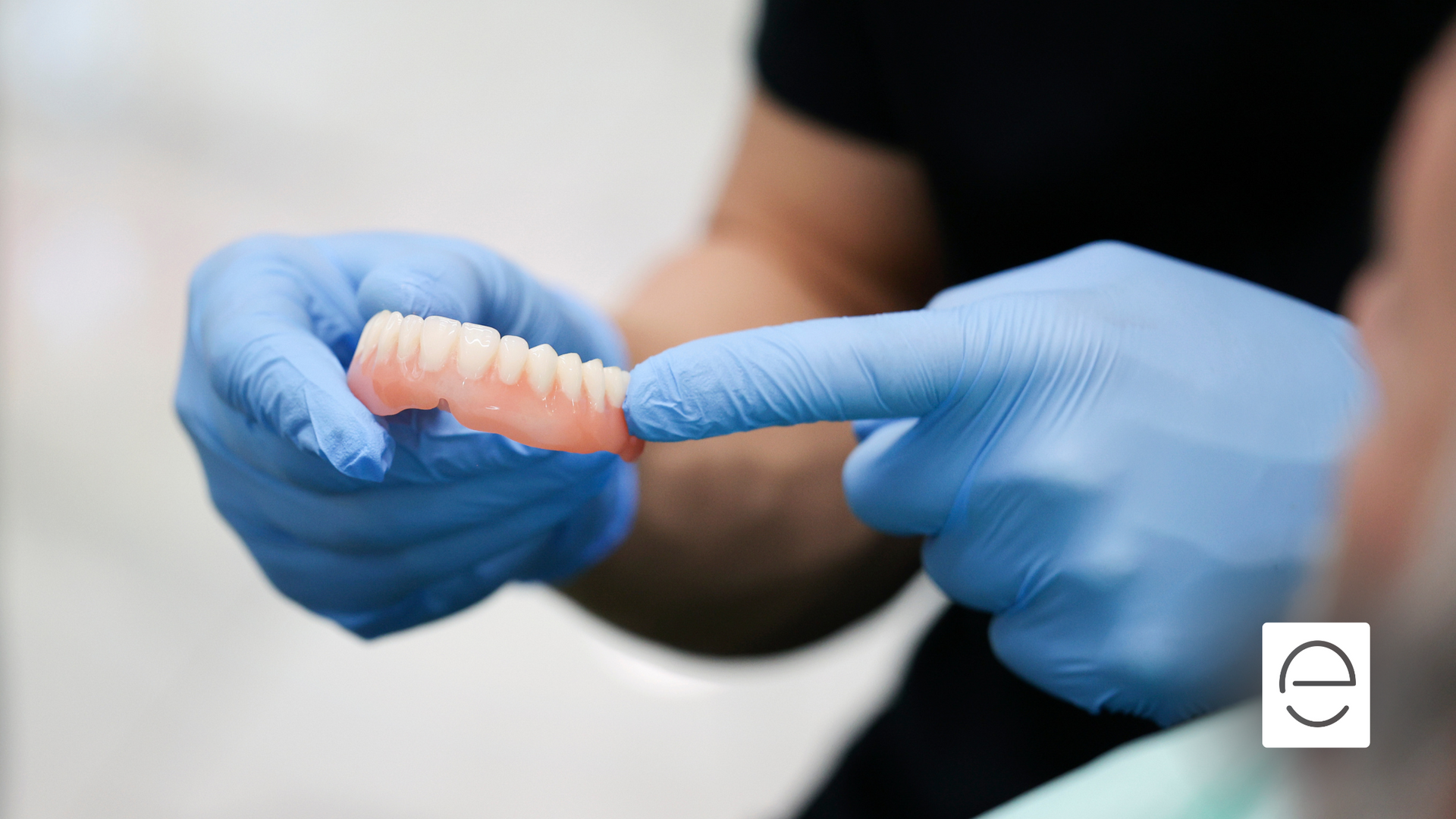 A person wearing blue gloves is holding a denture with their finger.