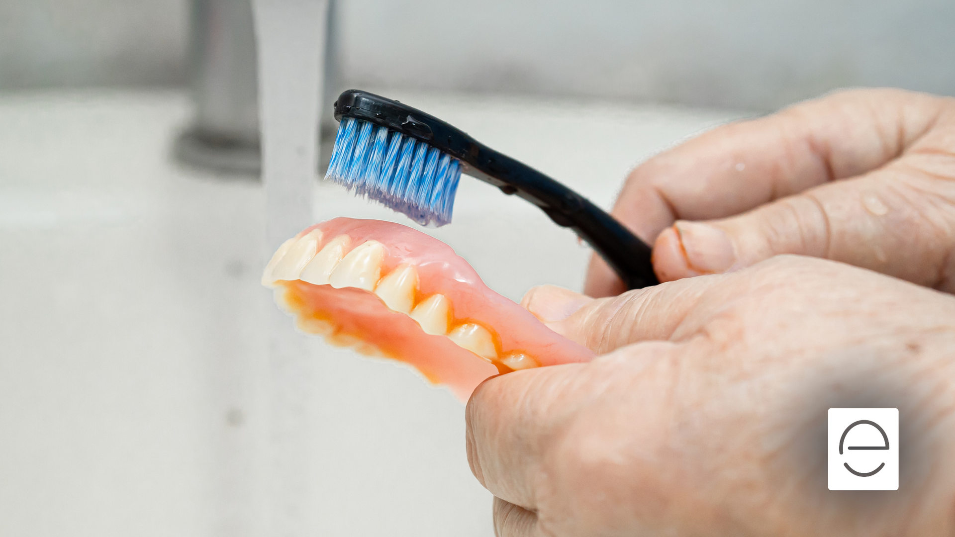 A person is brushing a denture with a toothbrush.