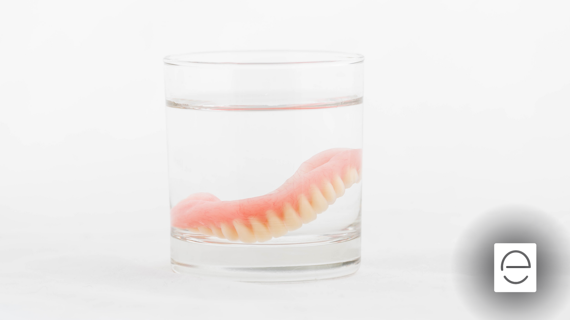 A denture is floating in a glass of water.