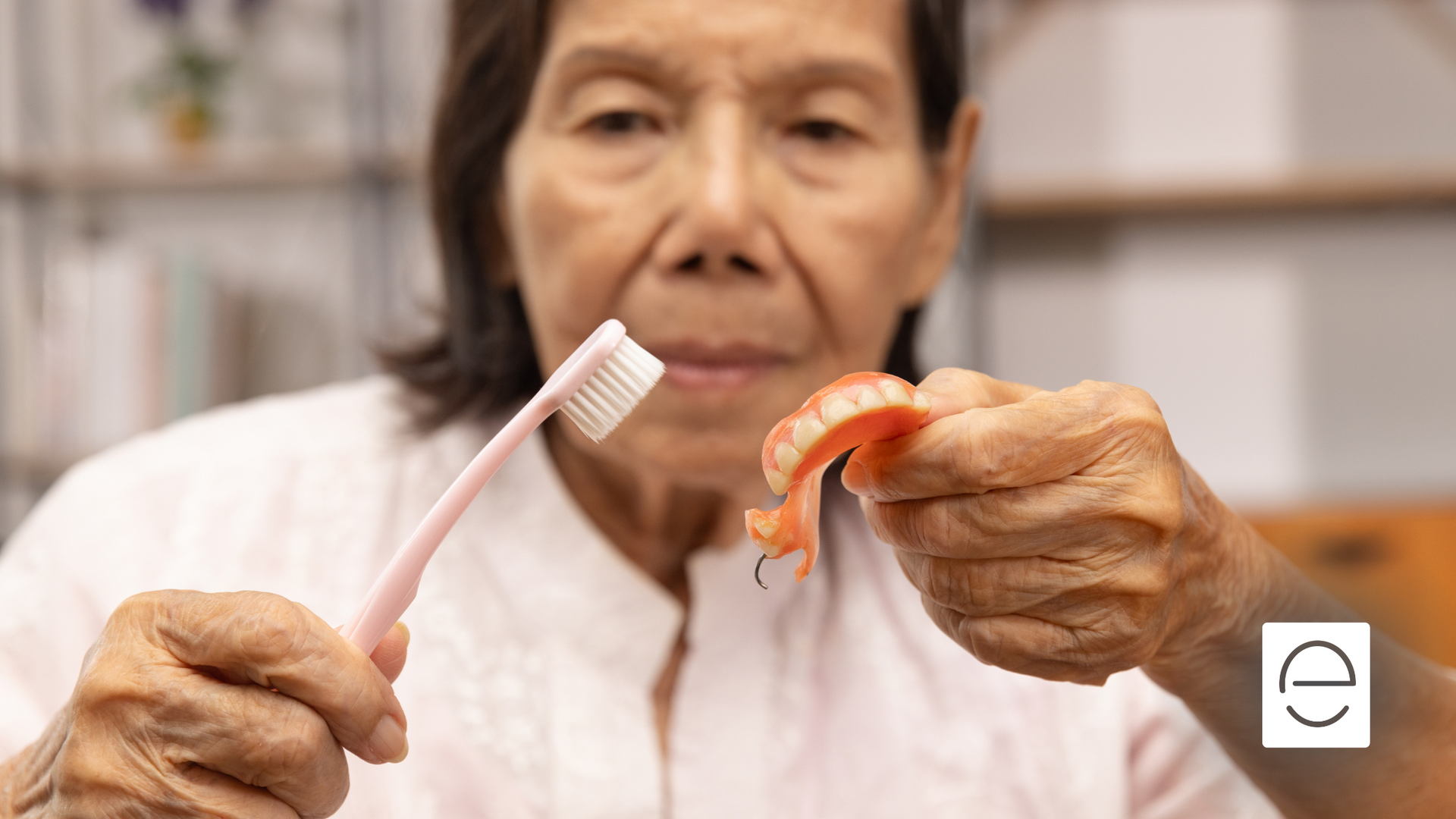 An elderly woman is brushing her dentures with a toothbrush.