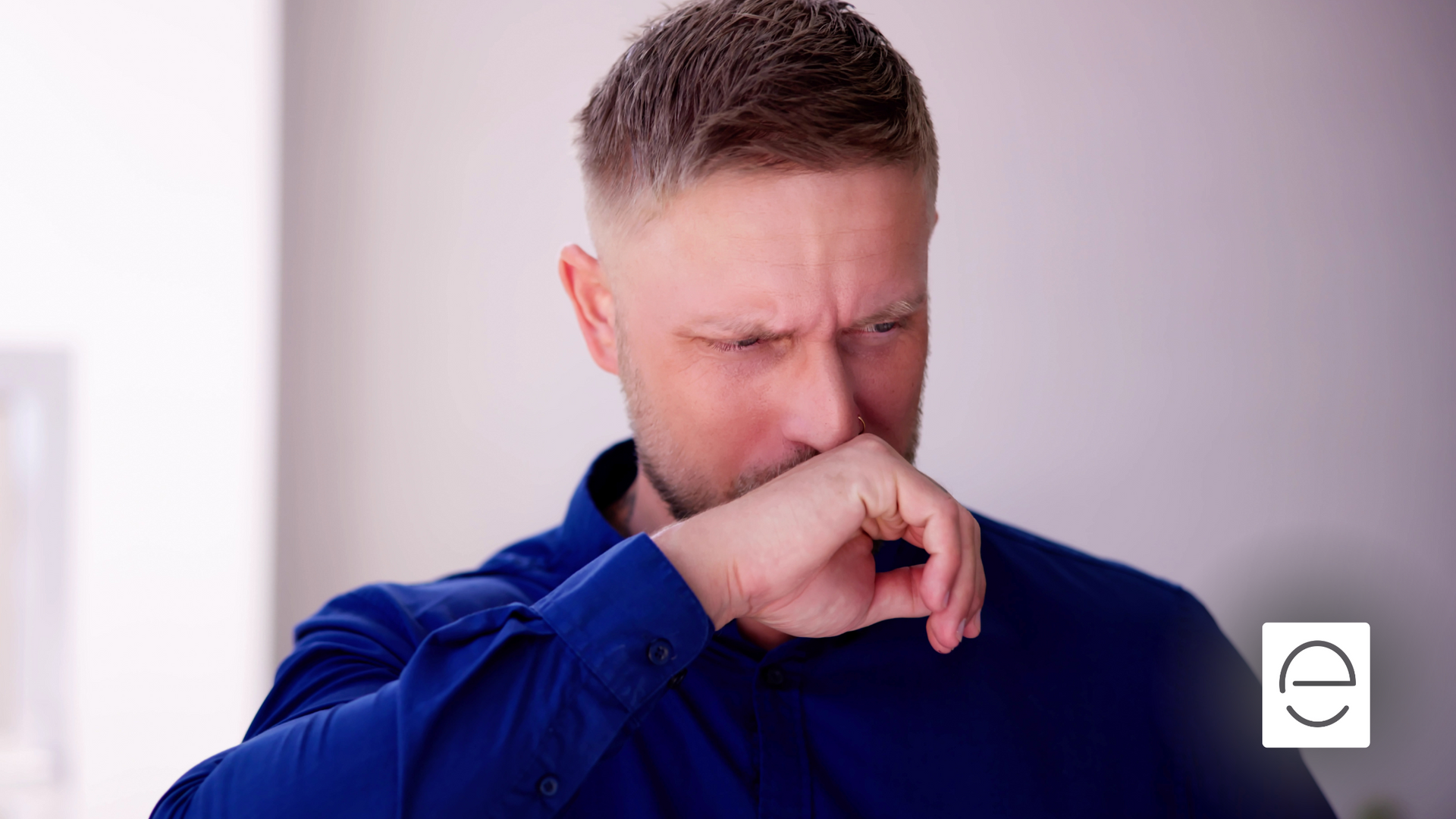 A man in a blue shirt is covering his nose with his hand.