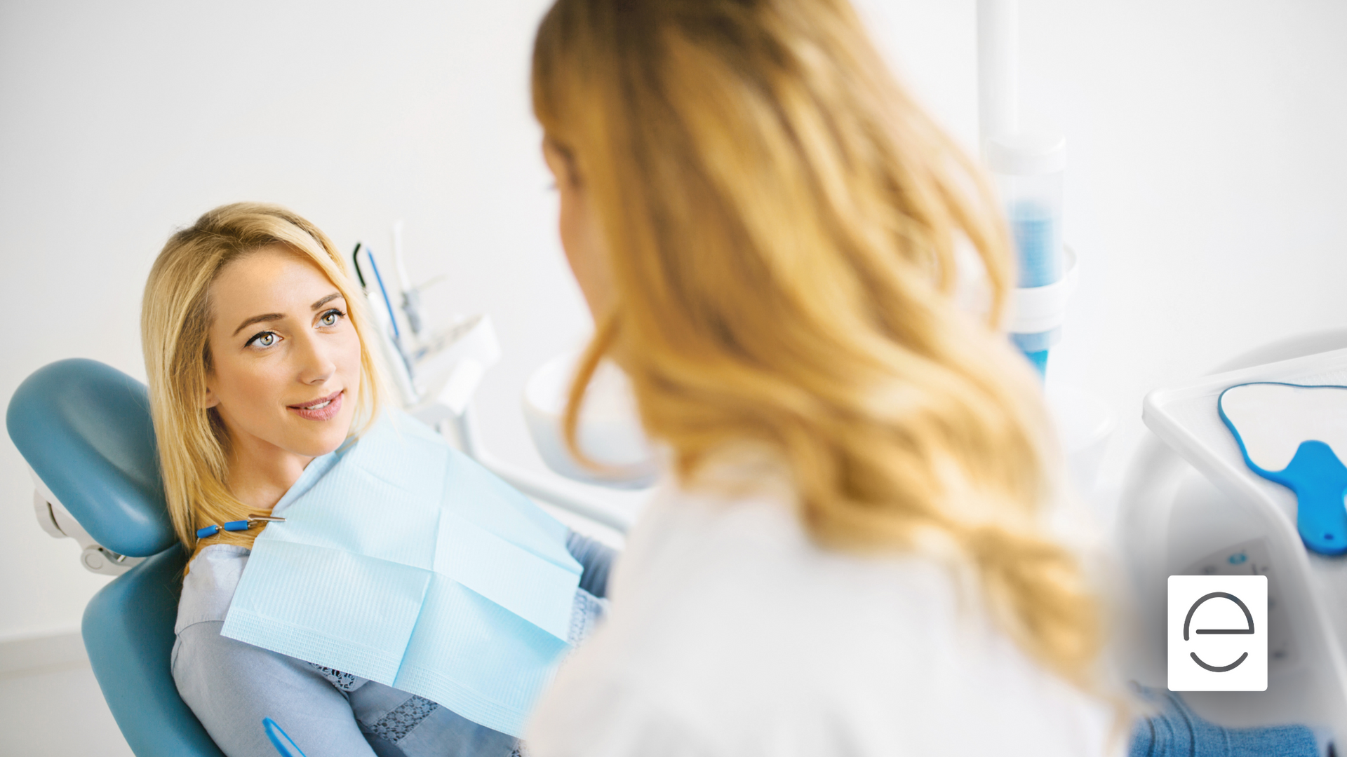 A woman is sitting in a dental chair talking to a dentist.