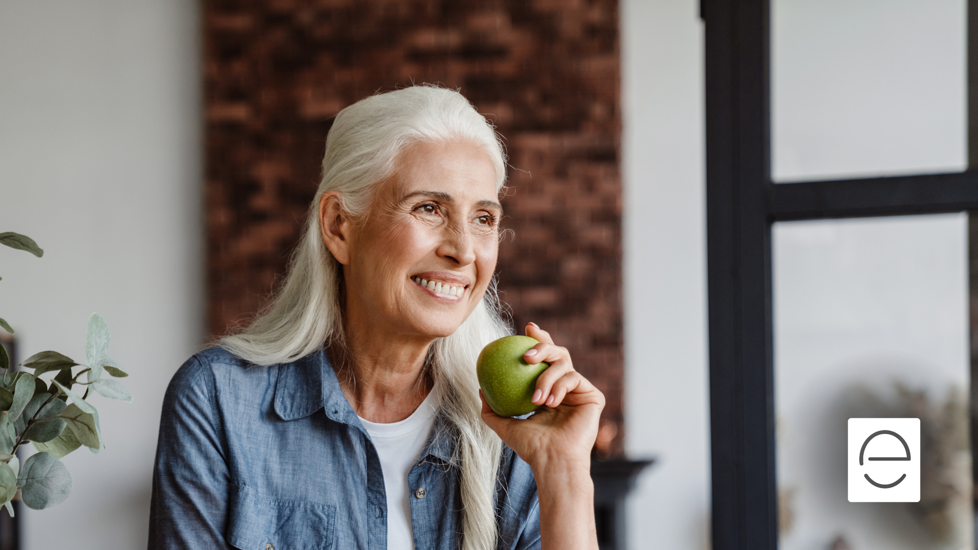 An elderly woman is eating an apple and smiling.