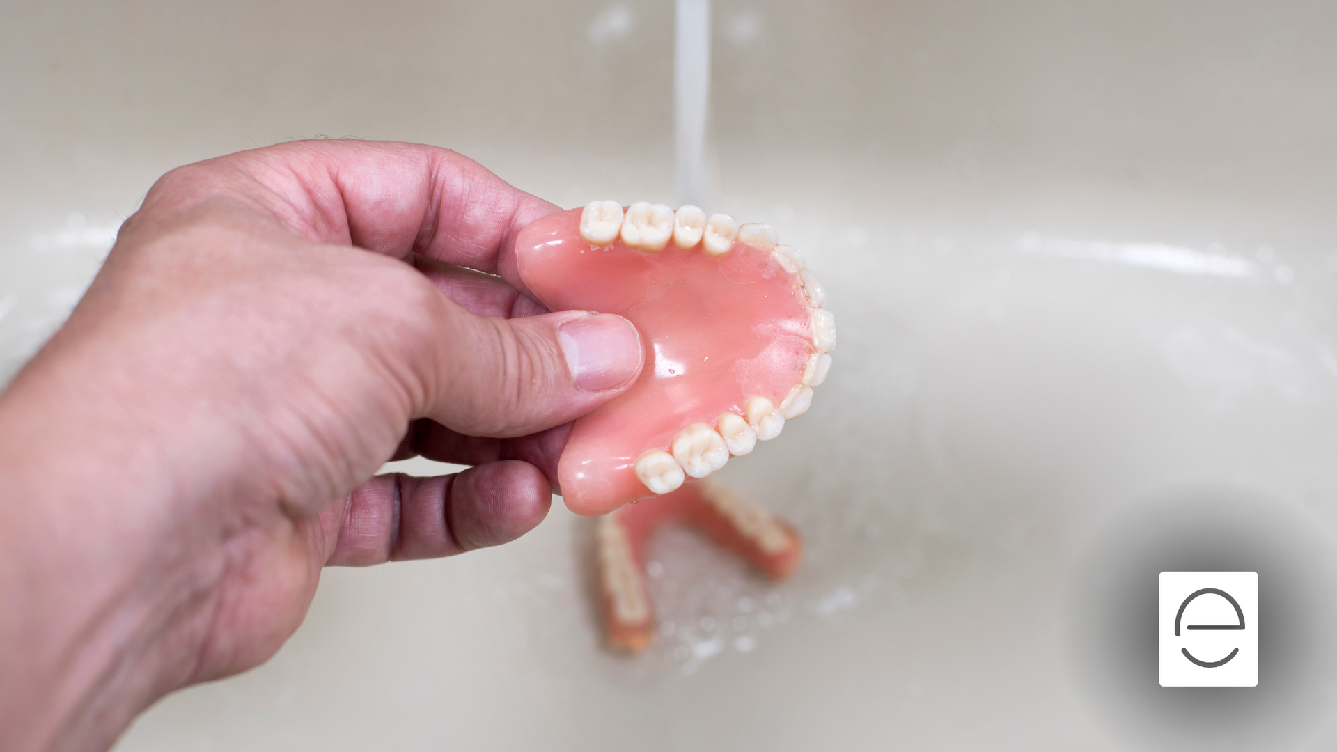 A person is washing a denture in a sink.