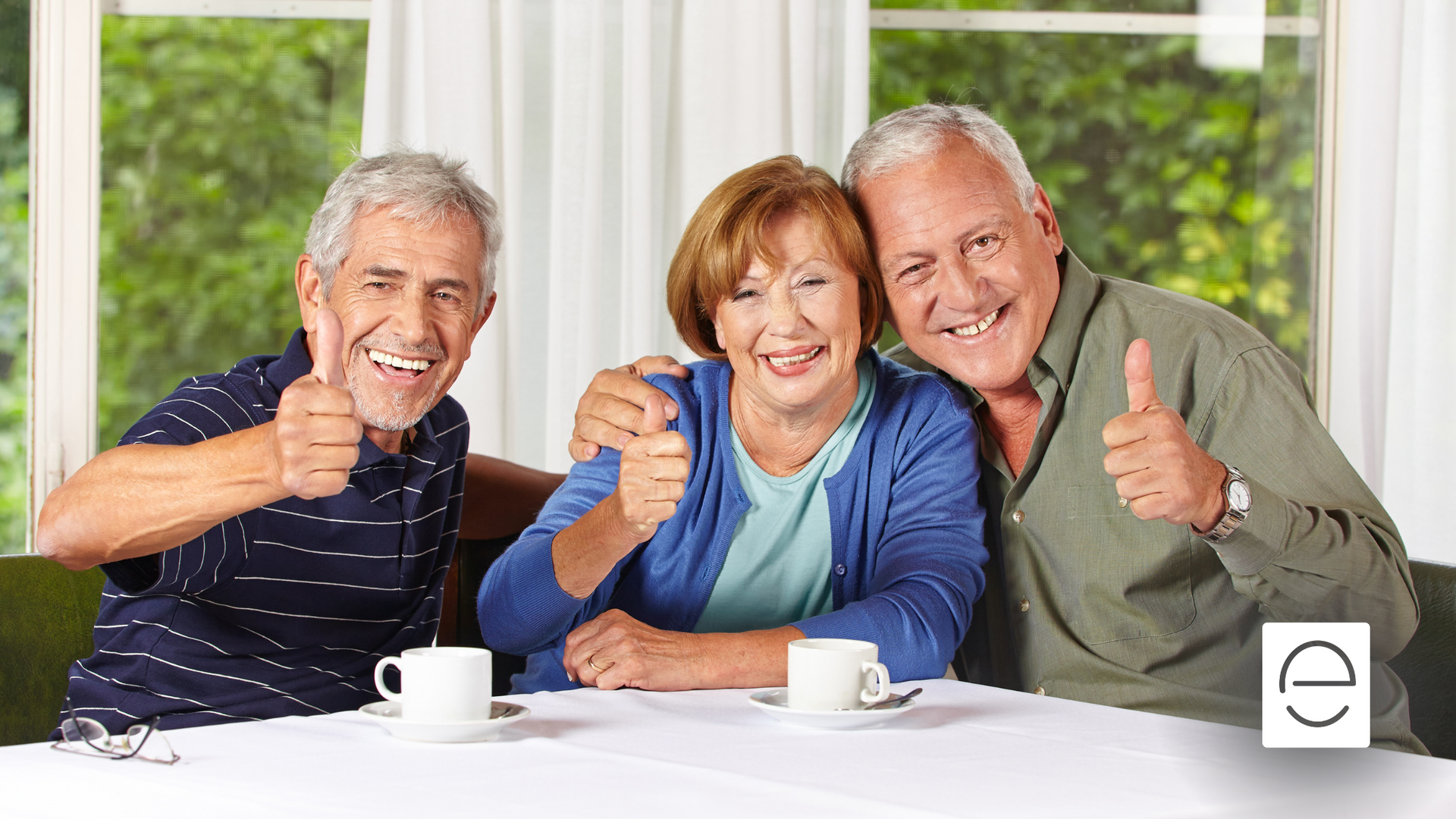 Three elderly people are sitting at a table giving a thumbs up.