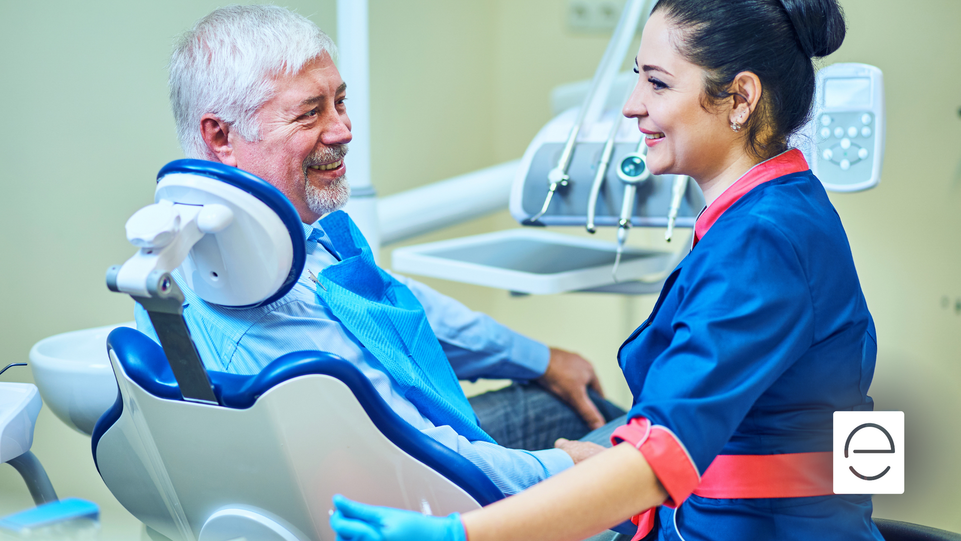 An older man is sitting in a dental chair talking to a female dentist.