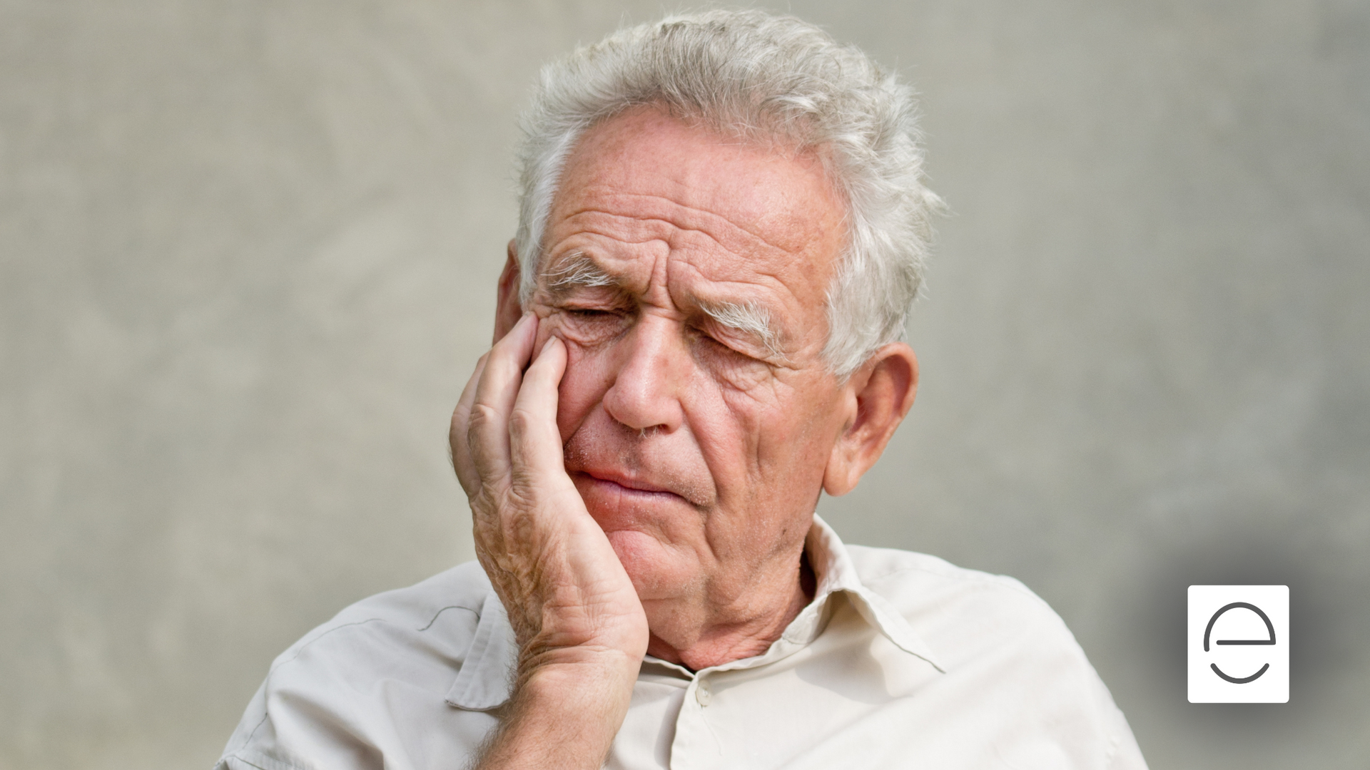An elderly man is holding his hand to his face.