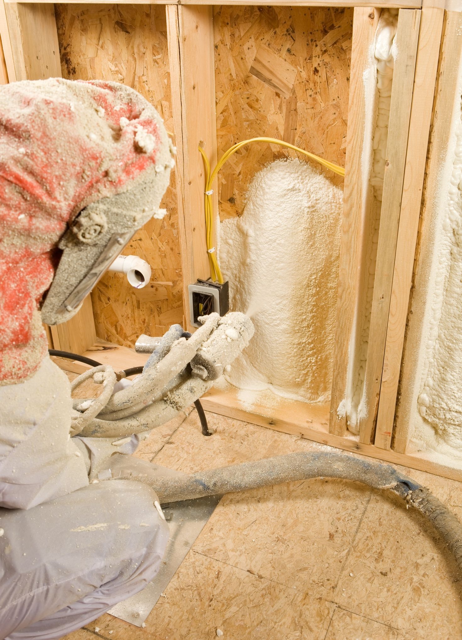 A man is spraying foam on a wall in a room.