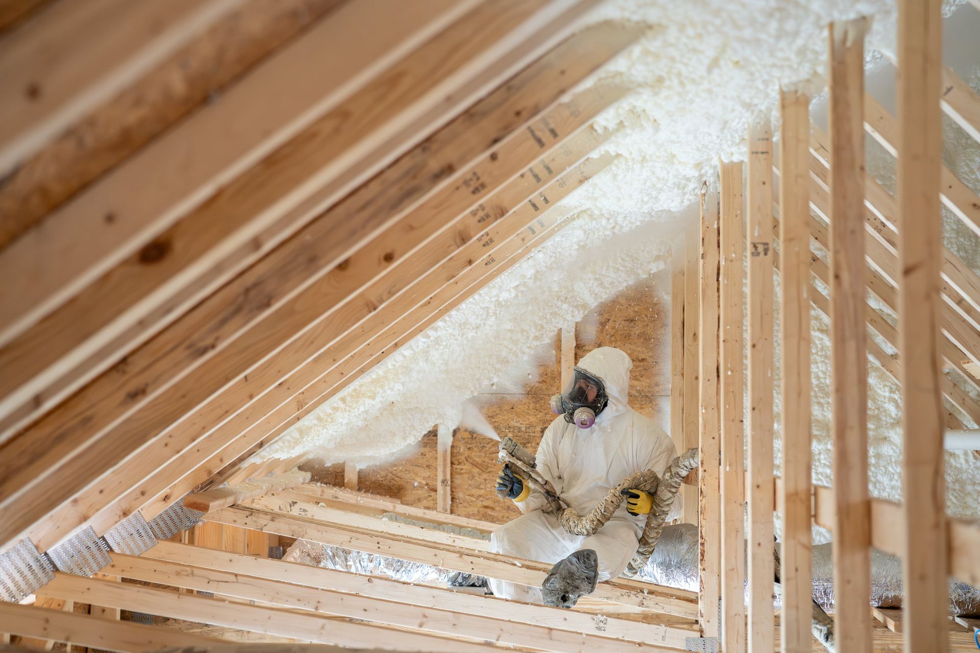 Construction worker in protective gear spraying house insulation. Construction worker in protective gear spraying house insulation.
