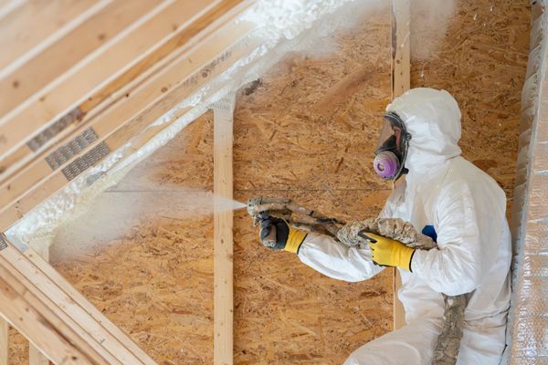 Worker spraying foam insulation on attic walls wearing protective gear. Worker spraying foam insulation on attic walls wearing protective gear.