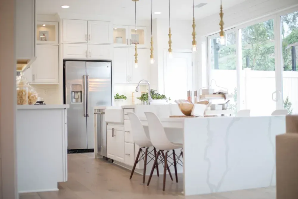 White modern kitchen with island, stainless steel fridge, and hanging lights.