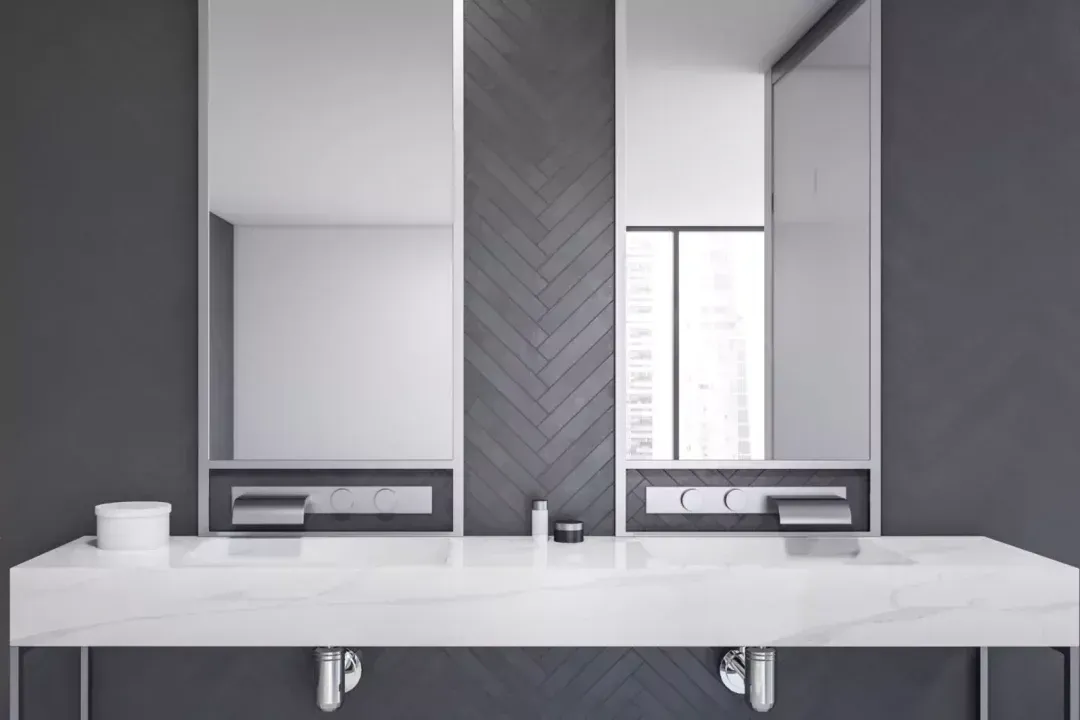 Bathroom with dual sinks, mirrors, and gray walls. White countertop and dark wood chevron accent.