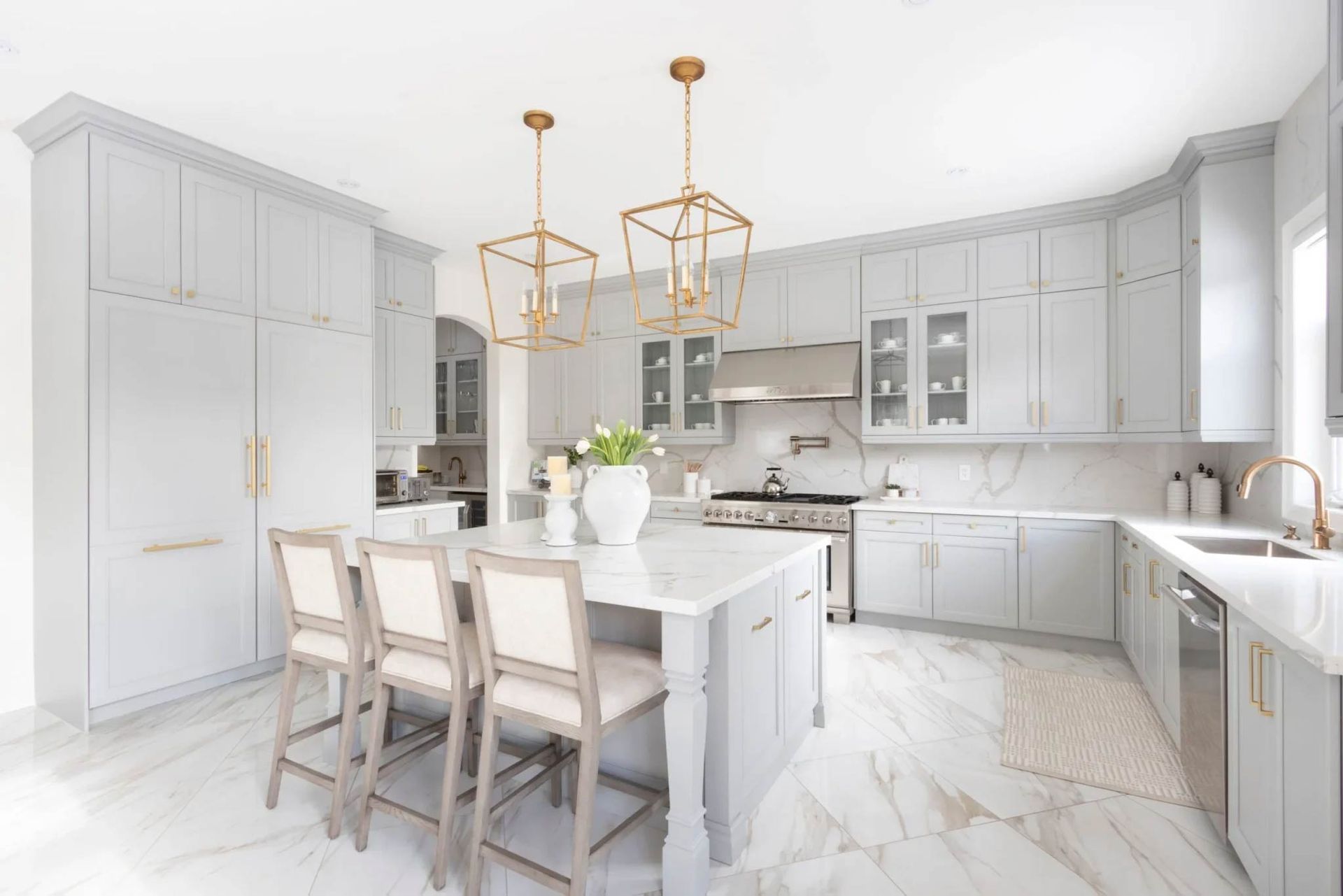 Elegant, light gray kitchen with marble accents, gold fixtures, and a central island with seating.