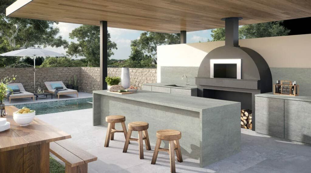 Outdoor kitchen with pool, pizza oven, bar seating, and wooden picnic table.