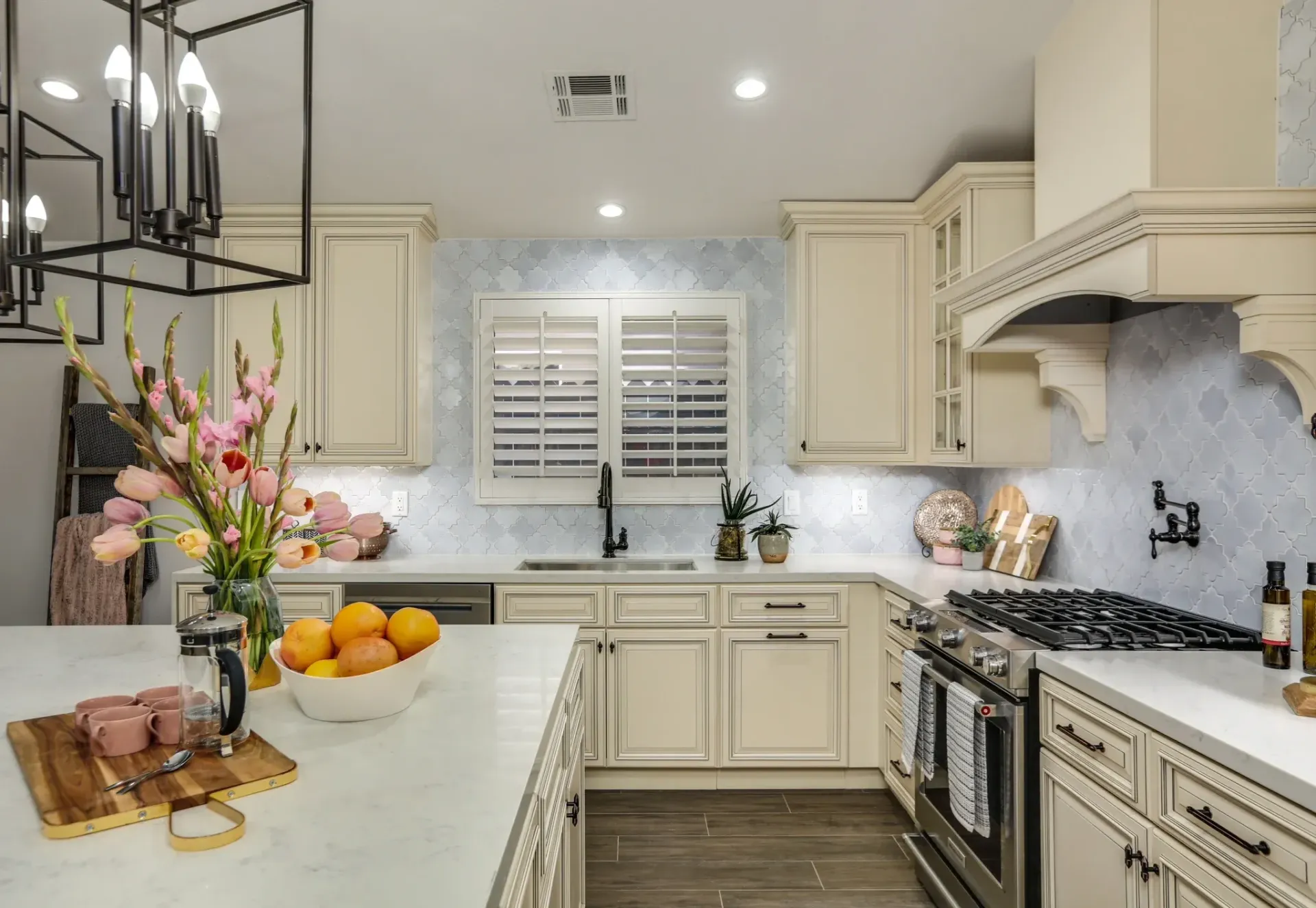 Cream-colored kitchen with white counters, light blue tiled backsplash, and large island with flowers and fruit.