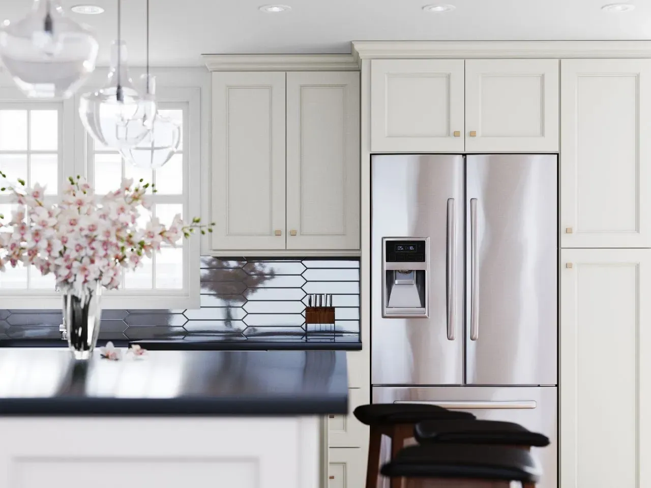 Cream-colored kitchen with stainless steel fridge, dark counter, and floral arrangement in front of a window.
