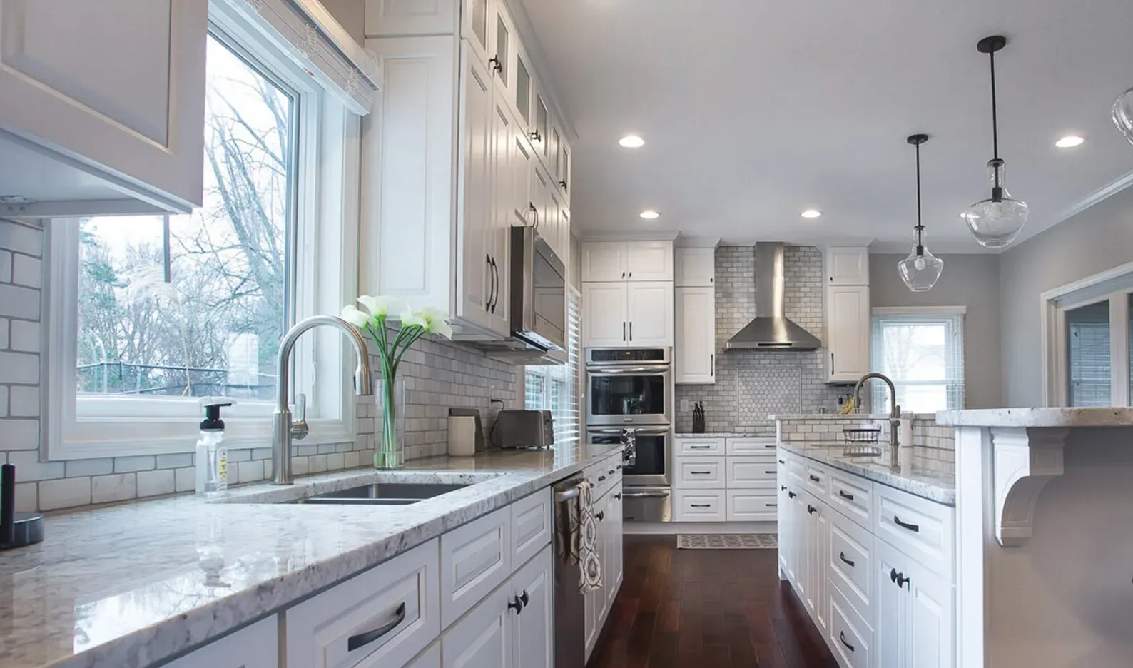Bright white kitchen with granite countertops, stainless steel appliances, and a large window.