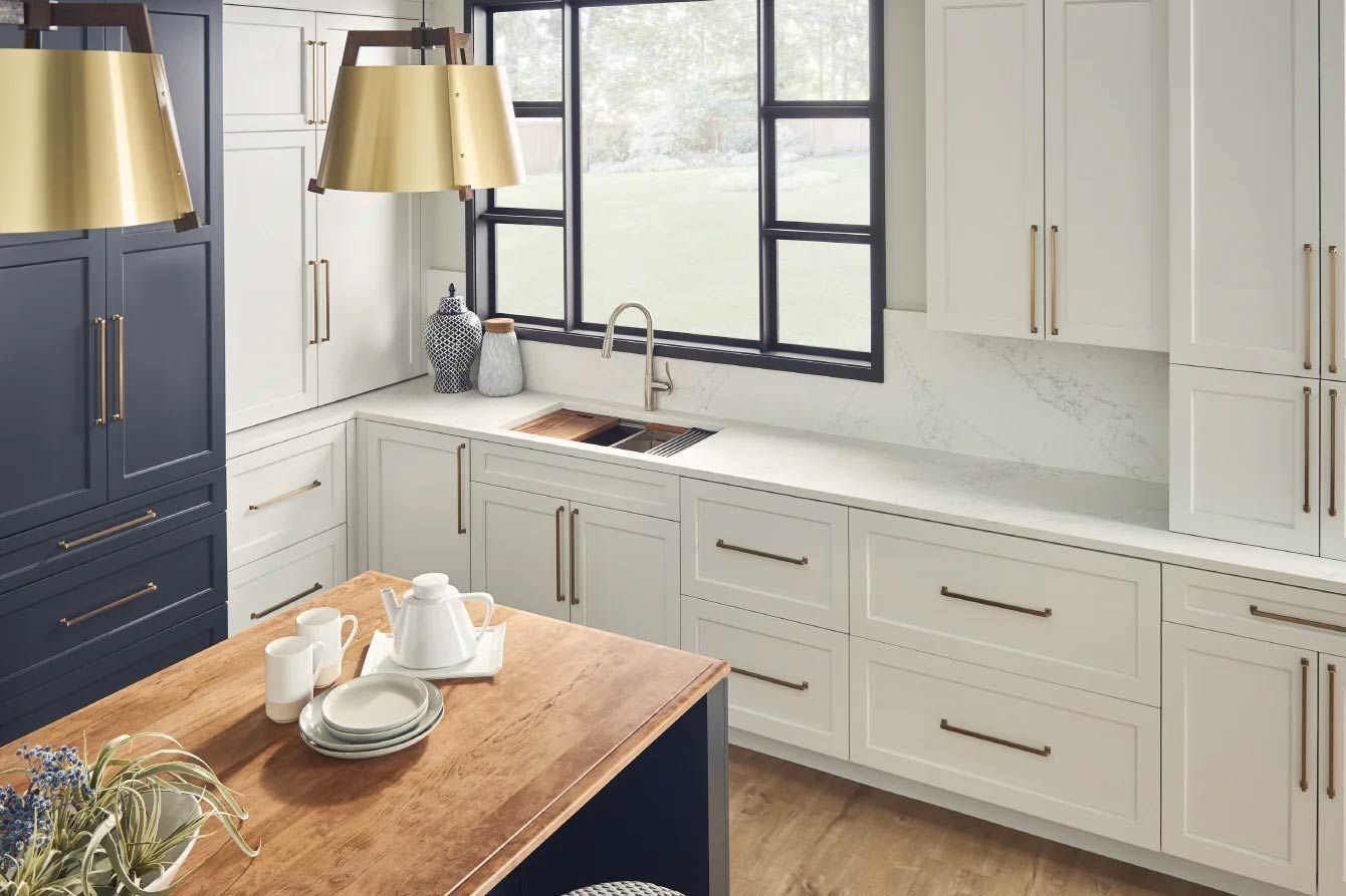 Kitchen with white and navy blue cabinets, wooden island, gold accents, and a window view.