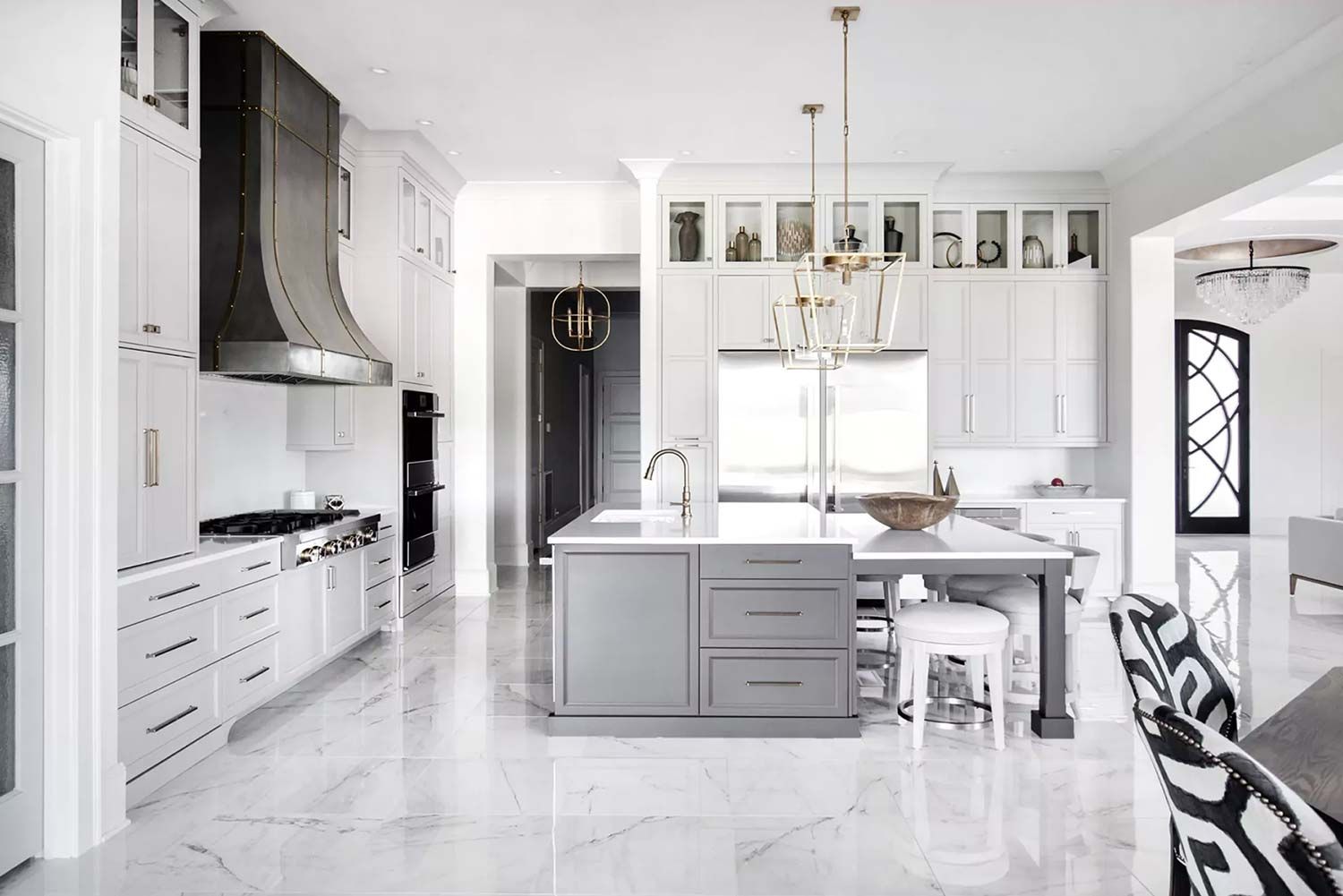 Bright white kitchen with a large island, stainless steel range hood, and marble flooring.