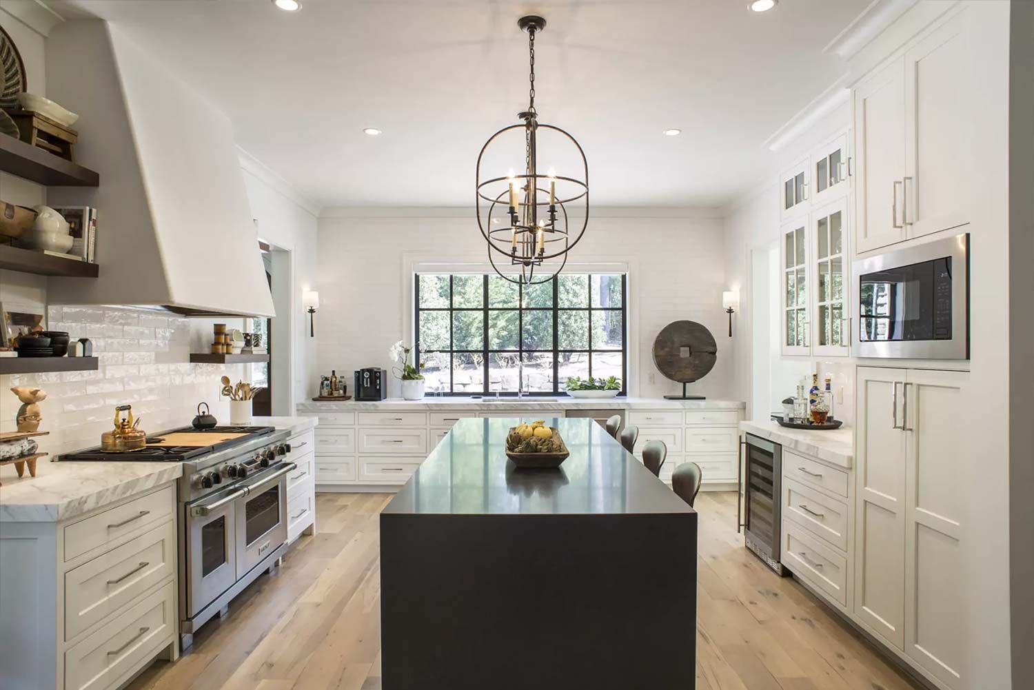 A modern kitchen with white cabinets, black island, and large window.