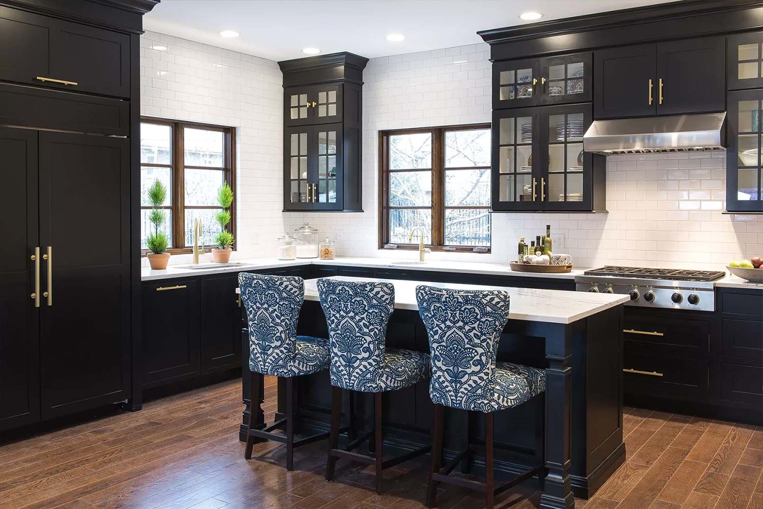 Black kitchen with island, white countertop, blue patterned barstools, and windows.