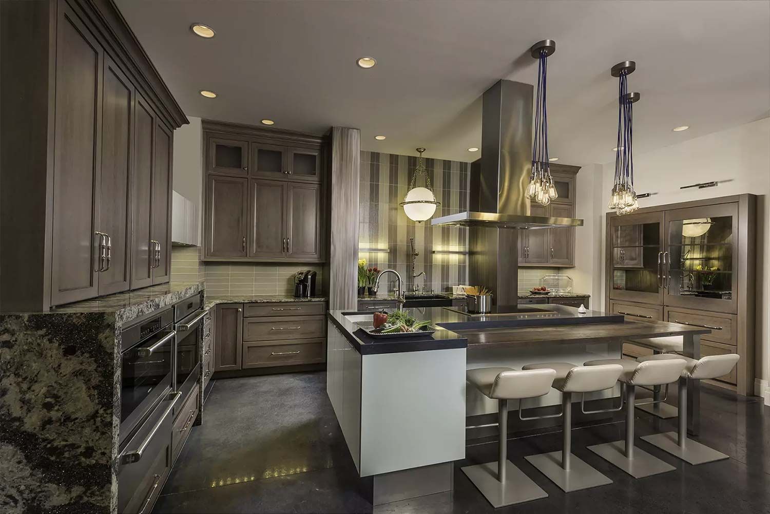 Modern kitchen with island seating, stainless steel range hood, and gray cabinets.